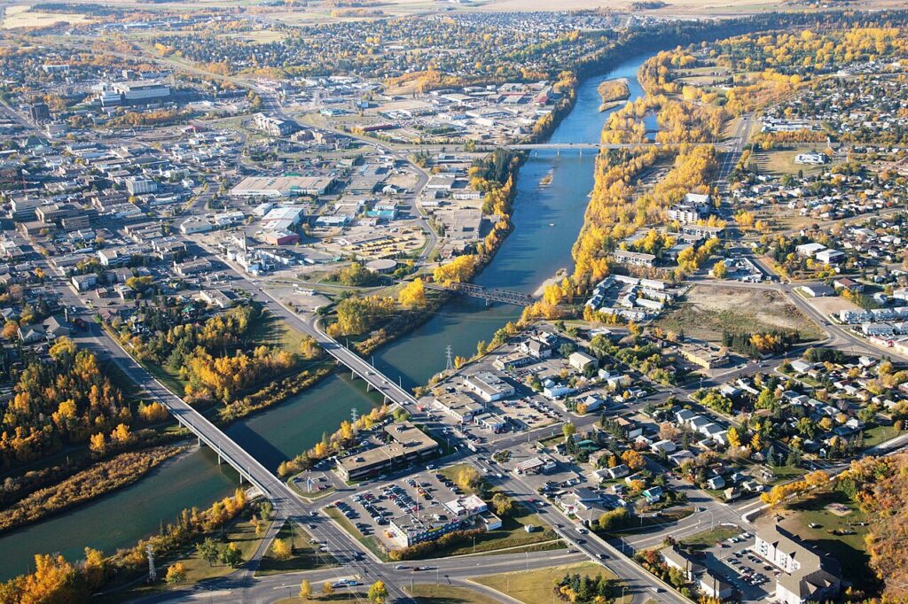 Vue aérienne de la ville de Red Deer, en Alberta, à l'automne : une rivière traverse la ville en deux et des ponts la traversent. Le centre-ville se trouve sur la gauche et les zones plus résidentielles se trouvent sur la droite. Les arbres (en grande partie des bouleaux trembles) sont devenus jaunes pour l'automne.