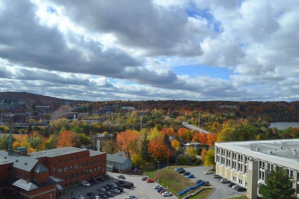 Une vue automnale de Sherbrooke, au Québec (bâtiments en brique au premier plan, avec un paysage urbain et des collines s'élevant derrière.)